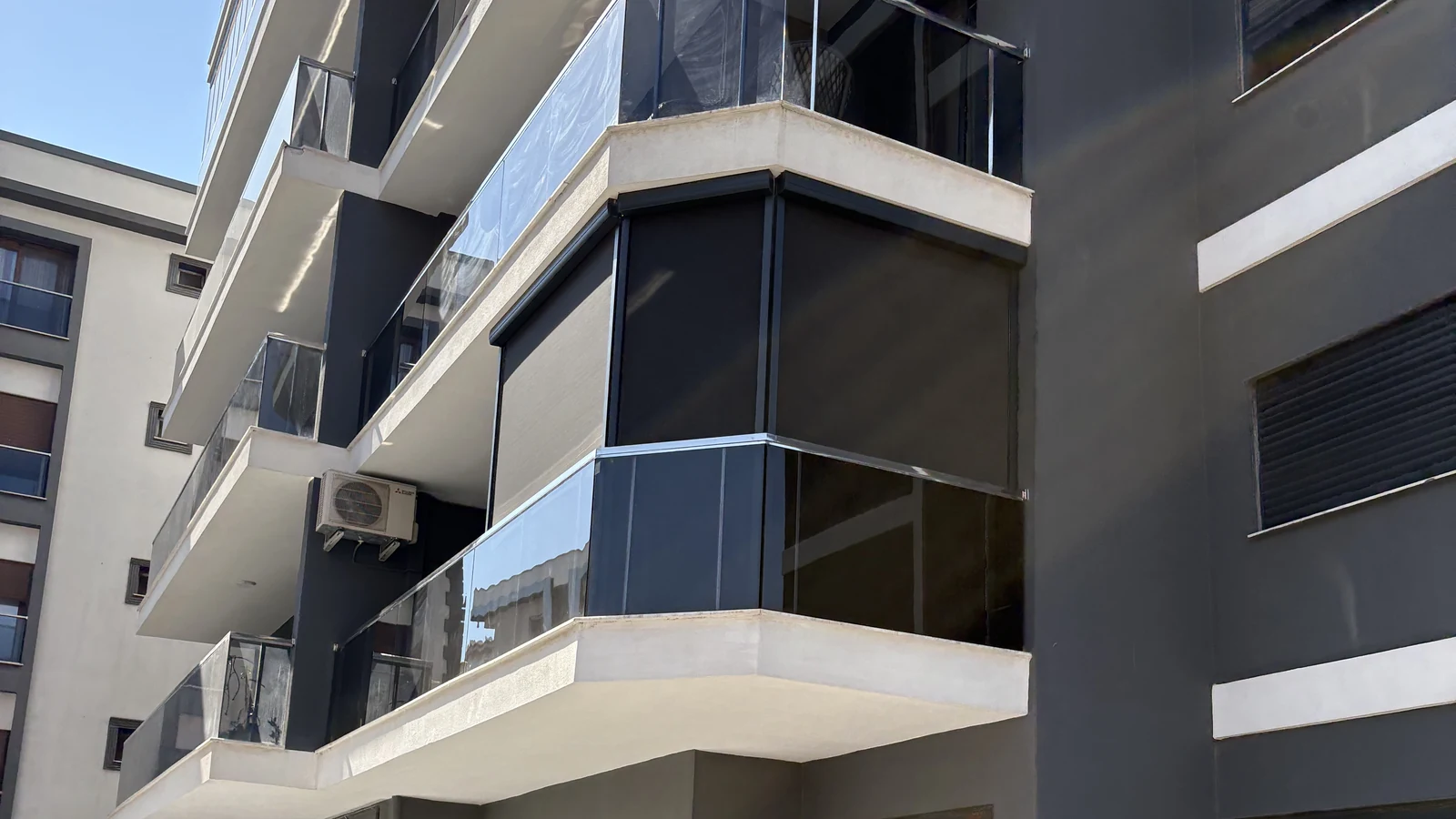 İzmir'de bir apartmanın köşe balkonlarına uygulanmış antrasit zip perde sistemleri