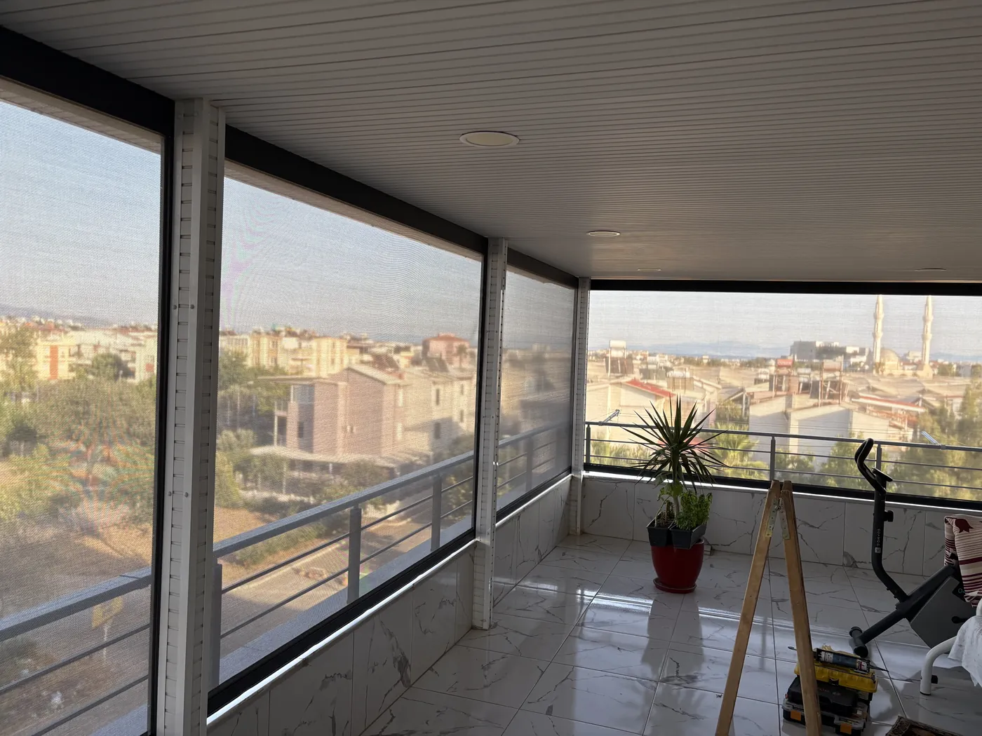 Zip perde inikken balkon içinden görünüm: üç cephede kumaş, arkada şehir manzarası