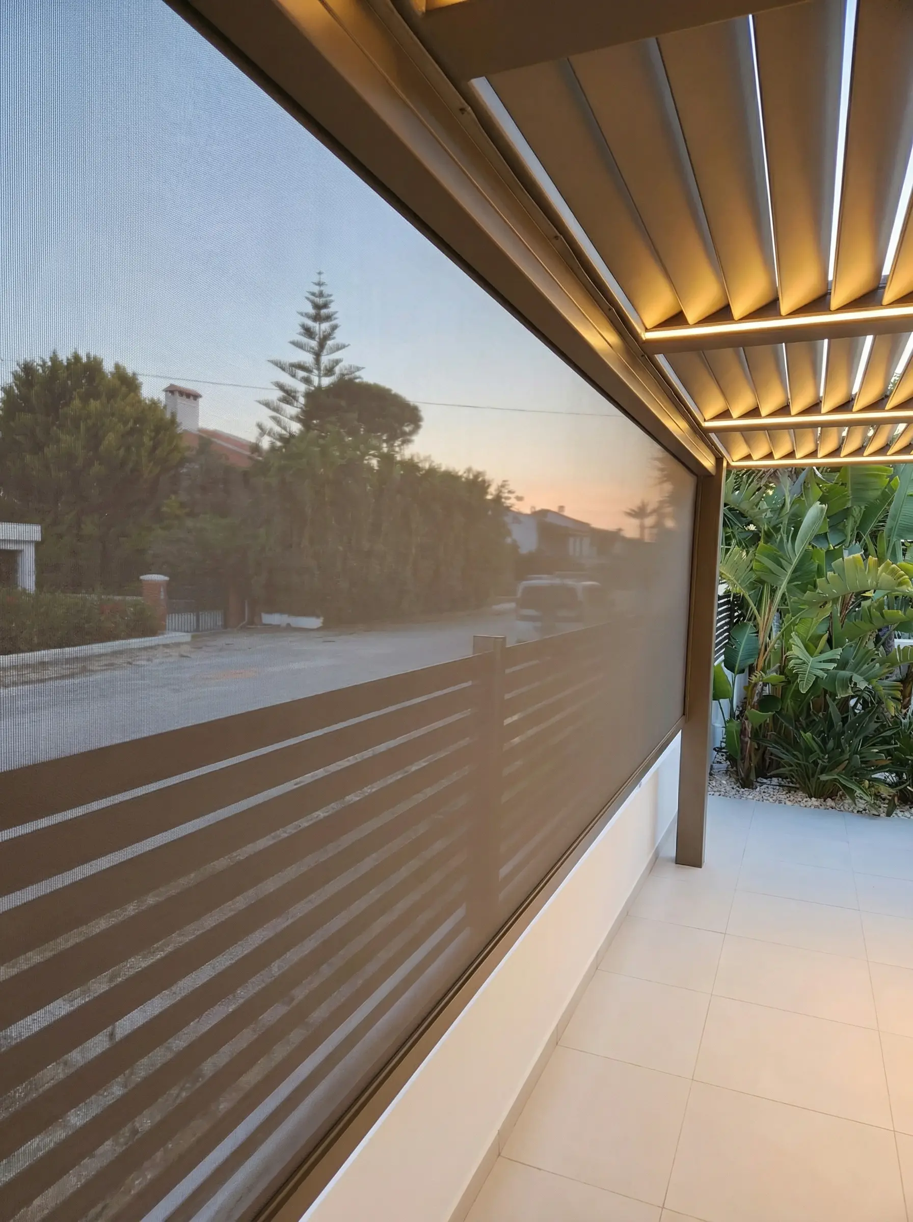 Screen kumaşın arkasından görünen sokak ve gün batımı, alüminyum pergola altında zip perde